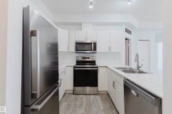 Modern kitchen featuring white cabinetry, light-toned countertops, and wood-finish flooring - 