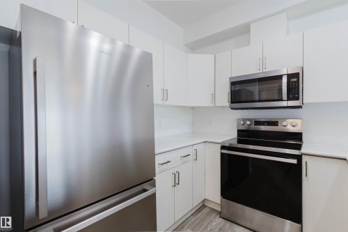 Modern kitchen featuring stainless steel appliances, white cabinetry with contemporary pulls, white countertops, and wood-finish flooring - 308 4316 139 Avenue, Edmonton, AB 