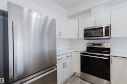 Modern kitchen featuring stainless steel appliances, white cabinetry with contemporary pulls, white countertops, and wood-finish flooring - 