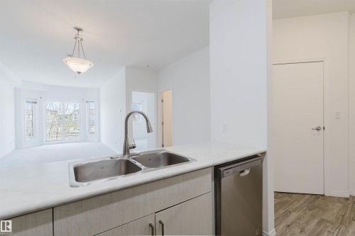 Kitchen counter featuring a double-basin stainless steel sink with a high-arc faucet, integrated dishwasher, and light wood-finish cabinetry - 308 4316 139 Avenue, Edmonton, AB 