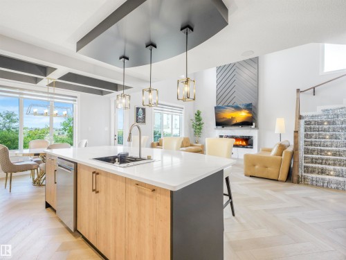 Open-concept interior featuring herringbone wood-finish flooring, a modern kitchen island with an undermount sink, and a contemporary fireplace with patterned wall detailing - 15 Elwyck Gate, Spruce Grove, AB - Indoor Photo Showing Kitchen With Upgraded Kitchen