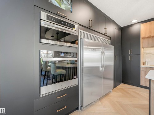 Modern kitchen featuring dark cabinetry with brushed gold hardware, integrated stainless steel appliances, and herringbone wood-finish flooring - 15 Elwyck Gate, Spruce Grove, AB - Indoor Photo Showing Other Room