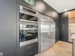 Modern kitchen featuring dark cabinetry with brushed gold hardware, integrated stainless steel appliances, and herringbone wood-finish flooring - 