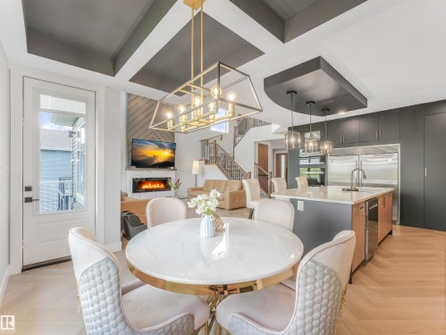 Open-concept interior featuring wood-finish herringbone flooring, a modern kitchen island with pendant lighting, a built-in fireplace, and a striking coffered ceiling design - 15 Elwyck Gate, Spruce Grove, AB - Indoor Photo Showing Dining Room