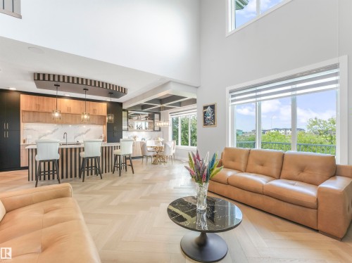 Open-concept living area featuring high ceilings, large windows, wood-finish herringbone flooring, a built-in kitchen island with pendant lighting, and a dining area with a coffered ceiling - 15 Elwyck Gate, Spruce Grove, AB - Indoor Photo Showing Living Room