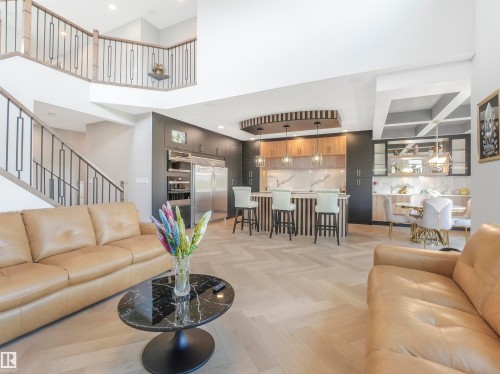 Open-concept living area featuring light wood-finish herringbone flooring, a two-story ceiling, and a modern kitchen with a waterfall island - 15 Elwyck Gate, Spruce Grove, AB - Indoor Photo Showing Living Room