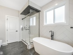 Modern bathroom featuring a freestanding soaking tub with a matte black floor-mounted faucet, a glass-enclosed shower with a rainfall showerhead, and contemporary gray tile flooring - 