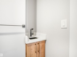 Modern vanity featuring a white countertop with a black basin, matte black faucet, and wood-finish cabinetry with brass-toned hardware - 