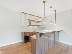 Contemporary wet bar featuring a beverage refrigerator, gold-toned hardware, white upper cabinetry, and a light wood-finish countertop - 