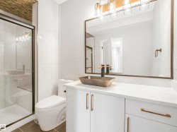 Modern bathroom featuring a glass-enclosed shower with white tiled walls, a floating vanity with a vessel sink, a large mirror, and a contemporary light fixture - 