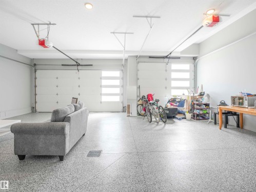 Spacious garage featuring two overhead doors with frosted glass panels, epoxy-coated flooring, ceiling-mounted lighting, and integrated garage door openers - 15 Elwyck Gate, Spruce Grove, AB - Indoor Photo Showing Garage
