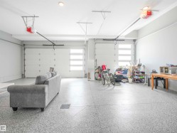 Spacious garage featuring two overhead doors with frosted glass panels, epoxy-coated flooring, ceiling-mounted lighting, and integrated garage door openers - 