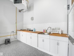 Utility space featuring speckled epoxy flooring, white cabinetry, and wood-finish countertops - 