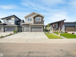 Contemporary two-story residence featuring a stone and siding exterior, a two-car garage with modern frosted glass inserts, and an expansive concrete driveway - 