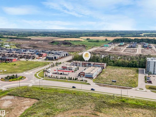 Aerial perspective showcasing a commercial building with an expansive paved parking lot, surrounded by developed residential areas and undeveloped land - 15 Elwyck Gate, Spruce Grove, AB - Outdoor With View