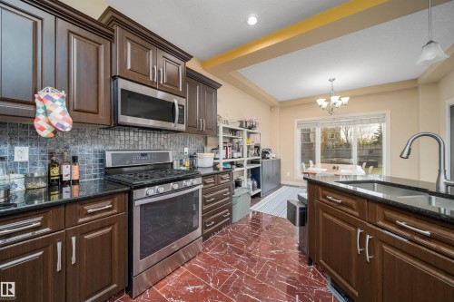 Kitchen featuring dark wood cabinetry, stainless steel appliances, black countertops, and a full tile backsplash - 1508 Cunningham Cape Cape, Edmonton, AB - Indoor Photo Showing Kitchen