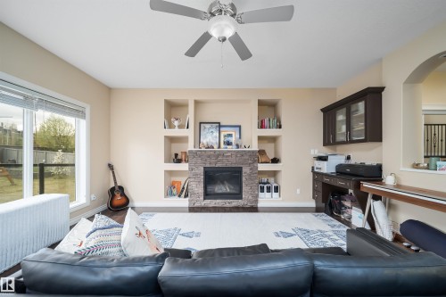 Spacious living area featuring a stone-clad fireplace with built-in shelving, wood-finish flooring, a ceiling fan, and a dedicated built-in desk area with overhead cabinetry - 1508 Cunningham Cape Cape, Edmonton, AB - Indoor Photo Showing Living Room With Fireplace