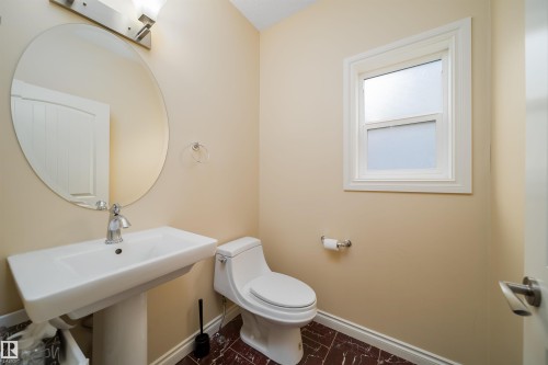 Pedestal sink with chrome faucet, complemented by a large circular mirror and overhead vanity lighting - 1508 Cunningham Cape Cape, Edmonton, AB - Indoor Photo Showing Bathroom