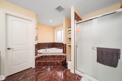 Bathroom featuring a corner soaking tub with tiled surround, a separate shower with a sliding glass door, and rich brown tiled flooring - 1508 Cunningham Cape Cape, Edmonton, AB - Indoor Photo Showing Bathroom