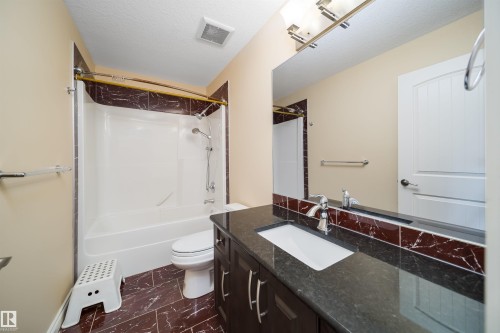 Full bathroom featuring a dark wood-finish vanity with a dark countertop and integrated sink, a large mirror, a shower-over-tub combination with a curved shower rod, and brown tile flooring - 1508 Cunningham Cape Cape, Edmonton, AB - Indoor Photo Showing Bathroom