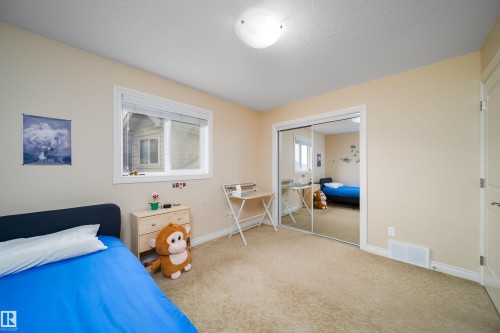 Carpeted bedroom featuring a large window, mirrored closet doors, a neutral wall color, white baseboards, and a flush-mount ceiling light - 1508 Cunningham Cape Cape, Edmonton, AB - Indoor Photo Showing Bedroom