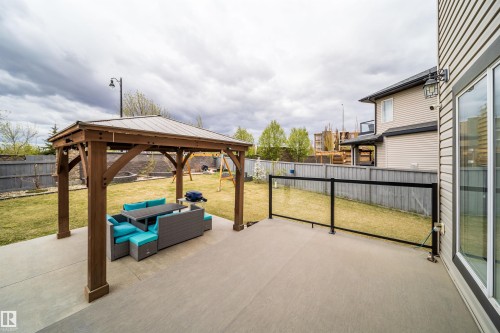 Expansive concrete patio featuring a wood gazebo with a metal roof, glass railing, and a sliding glass door entry to the home - 1508 Cunningham Cape Cape, Edmonton, AB - Outdoor With Exterior