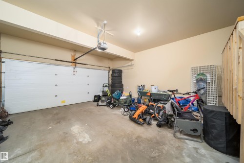 Spacious garage featuring a concrete floor, a white paneled garage door, an automatic garage door opener, and a single ceiling-mounted light fixture - 1508 Cunningham Cape Cape, Edmonton, AB - Indoor Photo Showing Garage