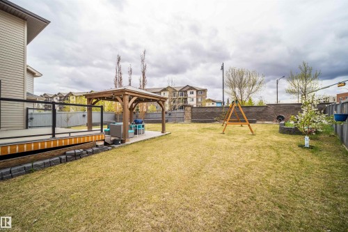 Expansive backyard featuring a built-in wooden deck with glass railing, a paved patio, and a freestanding pergola - 1508 Cunningham Cape Cape, Edmonton, AB - Outdoor