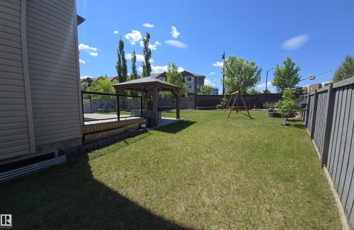 Expansive backyard featuring a manicured lawn, a raised wooden deck with glass panel railing, a built-in gazebo on a paver patio, and tall privacy fencing - 1508 Cunningham Cape Cape, Edmonton, AB 