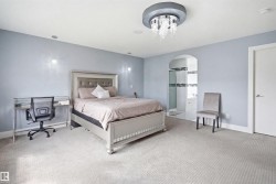 Spacious bedroom featuring light gray walls, recessed lighting, and a prominent crystal chandelier - 