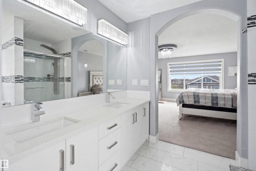 Contemporary bathroom featuring a double vanity with white cabinetry, light-toned countertops, and chrome fixtures - 3909 49 Ave, Beaumont, AB - Indoor Photo Showing Bathroom