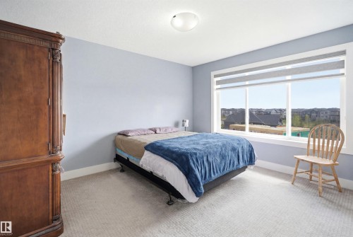 Spacious room featuring light blue walls, soft neutral carpeting, and a large window with roller shades - 3909 49 Ave, Beaumont, AB - Indoor Photo Showing Bedroom