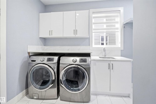 Dedicated laundry area featuring white shaker-style cabinetry, a built-in sink with a chrome faucet, and a light-colored countertop with a matching backsplash - 3909 49 Ave, Beaumont, AB - Indoor Photo Showing Laundry Room