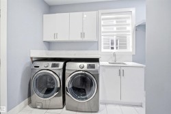 Dedicated laundry area featuring white shaker-style cabinetry, a built-in sink with a chrome faucet, and a light-colored countertop with a matching backsplash - 