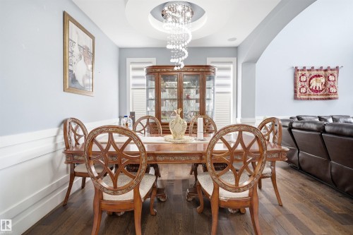 Dining area featuring a recessed ceiling with a contemporary chandelier, wainscoting, an arched doorway, and wood-finish flooring - 3909 49 Ave, Beaumont, AB - Indoor Photo Showing Dining Room