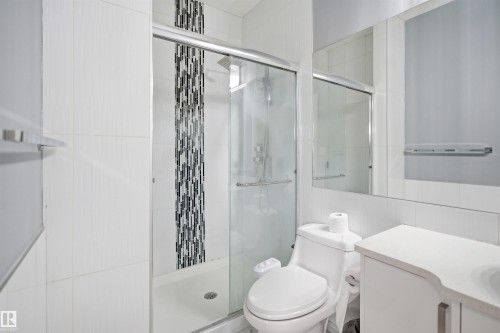 Contemporary bathroom featuring a glass-enclosed shower with a mosaic tile accent, a built-in vanity with a countertop, a toilet, and a wall-mounted mirror - 3909 49 Ave, Beaumont, AB - Indoor Photo Showing Bathroom