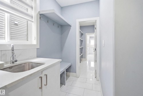 Utility area featuring a stainless steel sink, white stone-look countertop, and built-in white cabinetry - 3909 49 Ave, Beaumont, AB - Indoor