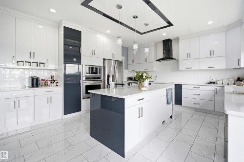 Contemporary kitchen featuring glossy white cabinetry with contrasting dark panels, an expansive island with a white countertop, and stainless steel appliances - 3909 49 Ave, Beaumont, AB - Indoor Photo Showing Kitchen With Upgraded Kitchen
