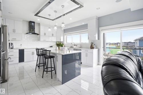 Modern kitchen featuring white cabinetry, a central island with countertop seating, stainless steel appliances, and large format tile flooring - 3909 49 Ave, Beaumont, AB - Indoor Photo Showing Kitchen With Upgraded Kitchen