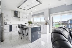 Modern kitchen featuring white cabinetry, a central island with countertop seating, stainless steel appliances, and large format tile flooring - 