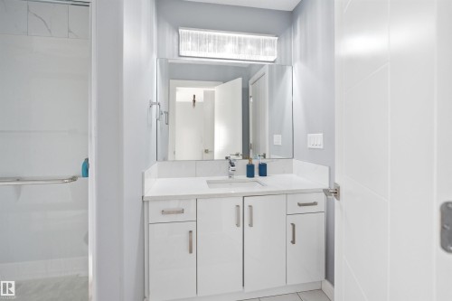 Contemporary bathroom featuring a white vanity with integrated sink, quartz countertop, and a large mirror with overhead lighting - 3909 49 Ave, Beaumont, AB - Indoor Photo Showing Bathroom