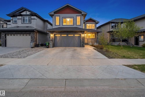 Two-story residence featuring gray siding, stone accents, a dark shingled roof, an attached two-car garage with carriage-style doors, and a concrete driveway - 3909 49 Ave, Beaumont, AB - Outdoor With Facade
