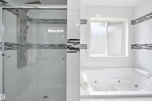 Modern bathroom featuring a glass-enclosed shower with a multi-jet panel, a jetted soaking tub, white tiled walls with decorative mosaic accents, and a frosted glass window - 3909 49 Ave, Beaumont, AB - Indoor Photo Showing Bathroom
