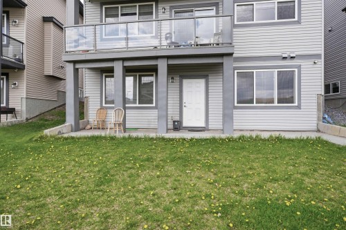 Ground-level patio with a white entry door, multiple windows, and a glass-paneled balcony overhead - 3909 49 Ave, Beaumont, AB - Outdoor