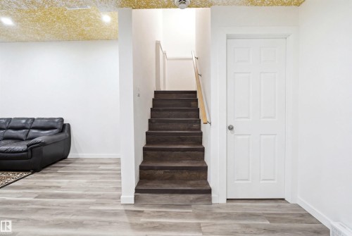 Staircase with wood-finish treads and light wood handrail, featuring white trim and a white paneled door - 3909 49 Ave, Beaumont, AB - Indoor Photo Showing Other Room