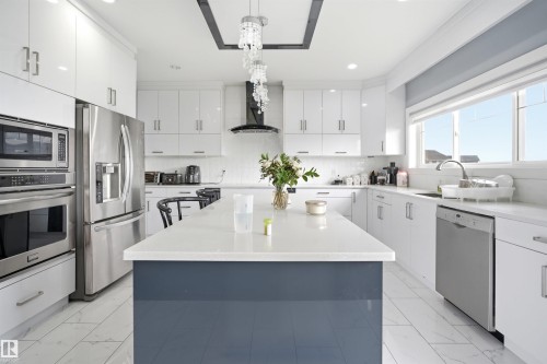 Contemporary kitchen featuring a large central island with a solid surface countertop, white cabinetry with silver-tone hardware, and stainless steel appliances - 3909 49 Ave, Beaumont, AB - Outdoor With Facade