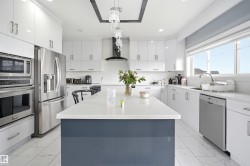 Contemporary kitchen featuring a large central island with a solid surface countertop, white cabinetry with silver-tone hardware, and stainless steel appliances - 