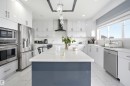 Contemporary kitchen featuring a large central island with a solid surface countertop, white cabinetry with silver-tone hardware, and stainless steel appliances - 3909 49 Ave, Beaumont, AB  - Outdoor With Facade 
