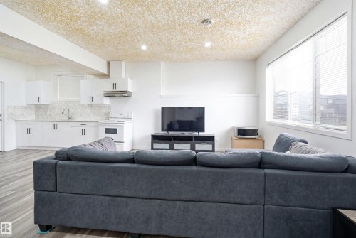 Open-concept living area featuring wood-finish flooring, a contemporary kitchen with white cabinetry and a patterned backsplash, white appliances, recessed lighting, and a large window with blinds - 3909 49 Ave, Beaumont, AB - Indoor Photo Showing Living Room