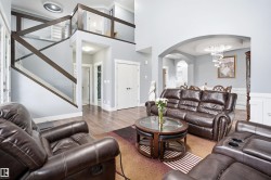 Open-concept living space featuring wood-finish flooring, a contemporary glass and wood railing staircase, arched doorways, tray ceiling with chandelier, and wainscoting - 